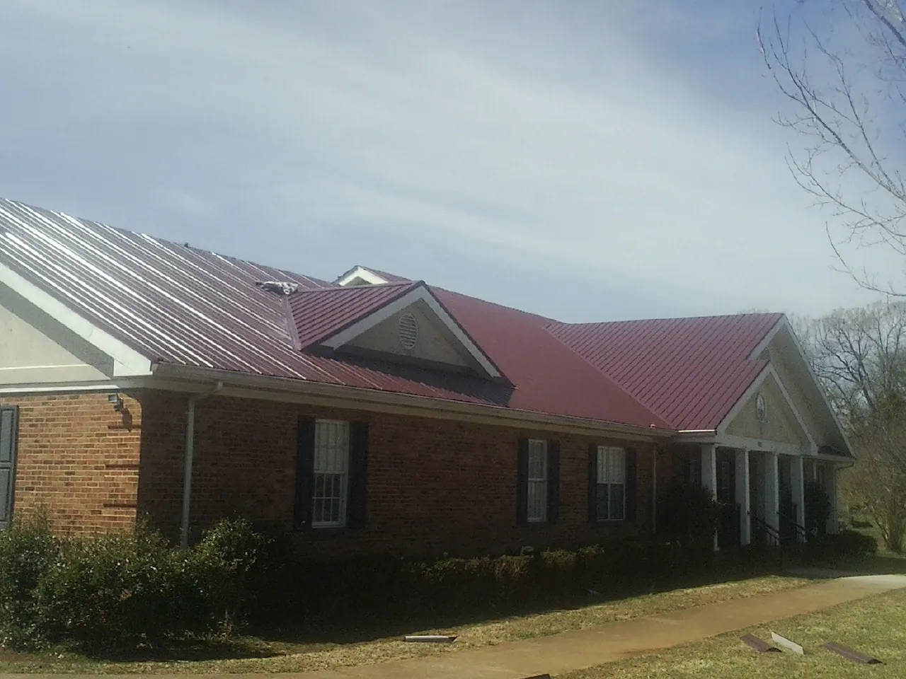 Red metal roof with gabled entries on a long brick building, from a Hail Damage Roof Repair job in Palo Alto
