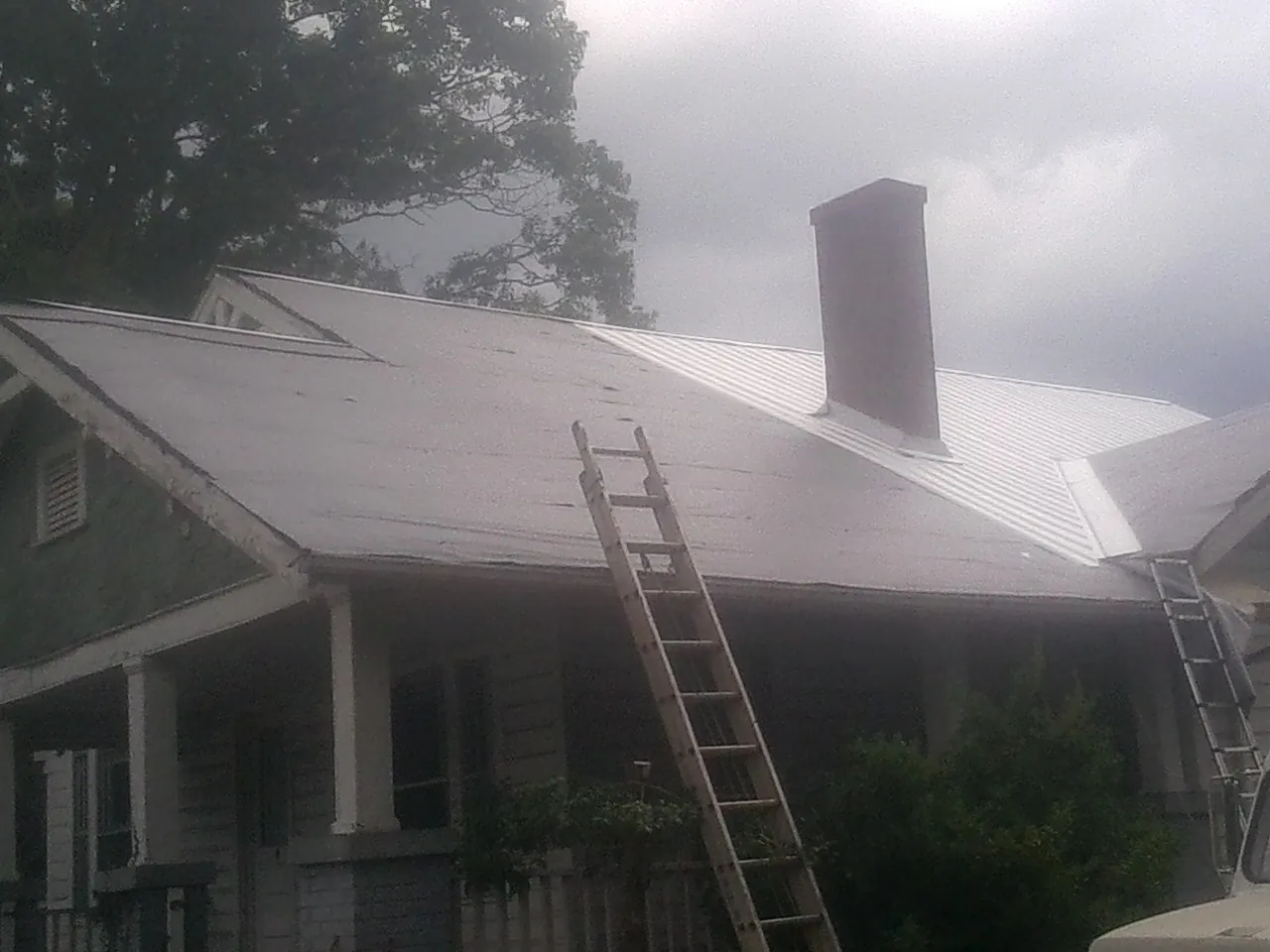 Ladders against a metal roof on an older home with a brick chimney in Palo Alto