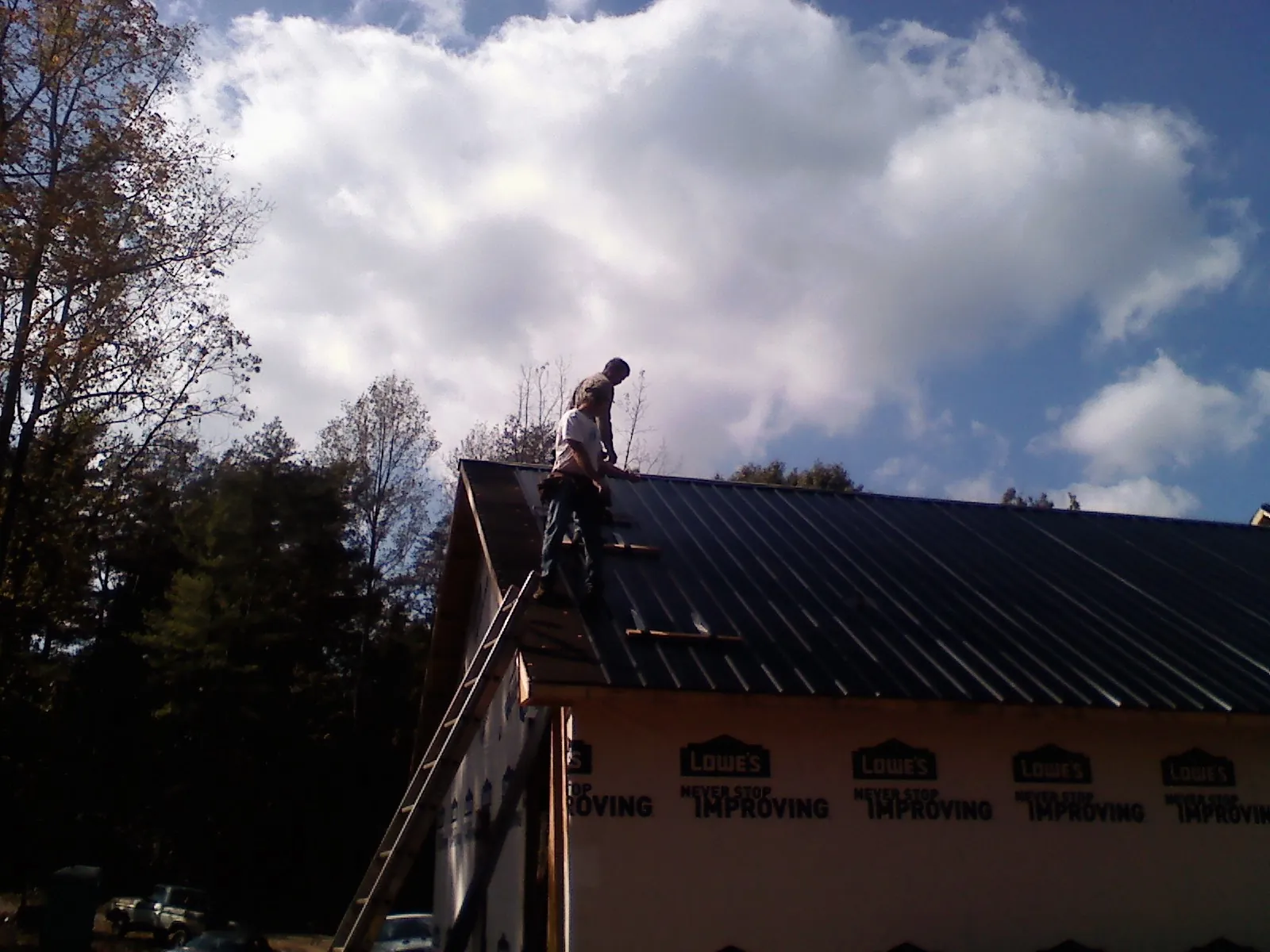 Roofer fastening dark metal panels high against a cloudy sky, from a Roof Inspection job in Palo Alto