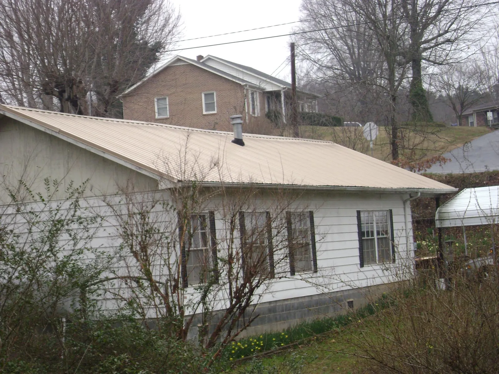 Tan metal roof on a white sided house set into a hillside — Commercial Roofing by Roofing Brothers in Palo Alto